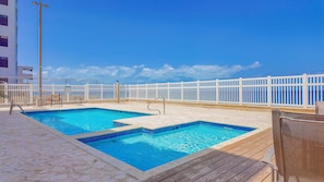 A swimming pool with a wooden deck and white railings, overlooking a clear blue sky and ocean. - Ocean front 2-bedroom condo in lovely Rincon with cool AC (Rincon)
