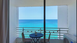 A balcony with a view of the ocean, a table, two chairs, and a potted plant. - Ocean front 2-bedroom condo in lovely Rincon with cool AC (Rincon)
