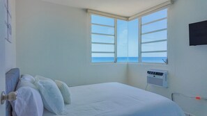 A bedroom with a bed, pillows, a window with a view of the sea, and a wall-mounted air conditioner. - Ocean front 2-bedroom condo in lovely Rincon with cool AC (Rincon)