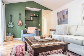 Ein Wohnzimmer mit einer Couch, einem Couchtisch, einer Gitarre und einem Bücherregal.