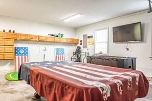 Ein Zimmer mit einem Bett, einem Kicker, einem Fernseher und einem Fenster mit Jalousien.