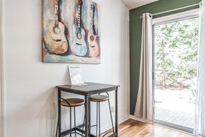 A room with a table and two stools, a painting of guitars on the wall, and a view through a glass door. - The Rocken Lake Hills Retreat (Pinehurst)