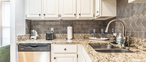 Una cocina con armarios blancos, encimeras de granito, lavavajillas, fregadero y salpicadero de azulejos.