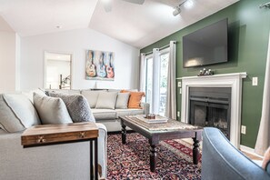 Un salon comprenant un canapé, une table basse, une cheminée et un téléviseur fixé au mur.