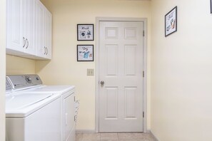 A laundry room with a white door, a washing machine, and two framed pictures on the wall. - The Rocken Lake Hills Retreat (Pinehurst)