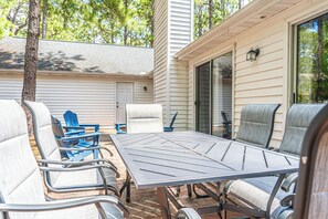 An outdoor patio with a metal table and chairs, a sliding glass door, and a view of a neighboring building. - The Rocken Lake Hills Retreat (Pinehurst)