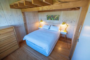 Une chambre à coucher aux murs lambrissés, avec un lit, deux tables de chevet et une petite table d’appoint.