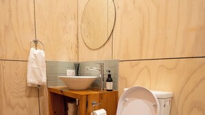 Et badeværelse med trægulv, toilet i hvidt, trækommode med vask og et spejl.