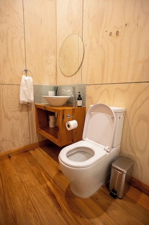 Une salle de bain avec un plancher en bois, des toilettes blanches, un meuble-lavabo en bois avec un évier et un miroir.