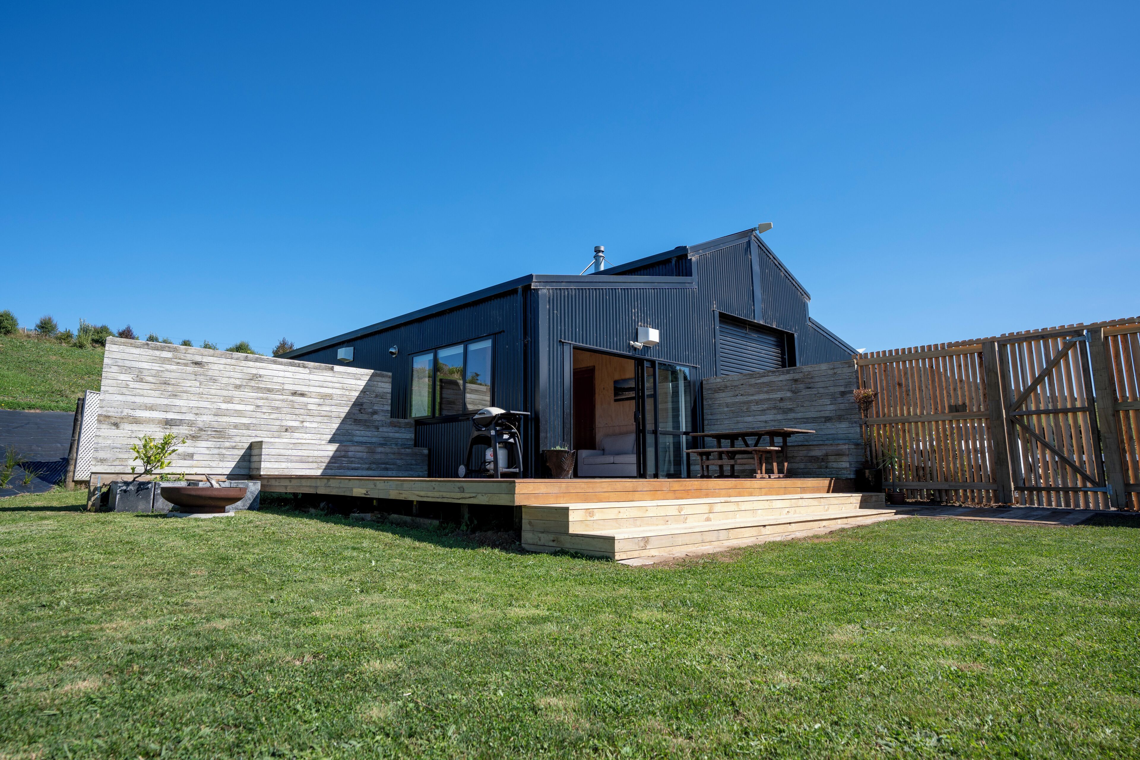 Une maison moderne dotée d’une terrasse en bois, d’un patio et d’un jardin clôturé.