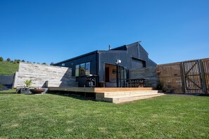 Une maison moderne dotée d’une terrasse en bois, d’un patio et d’un jardin clôturé.