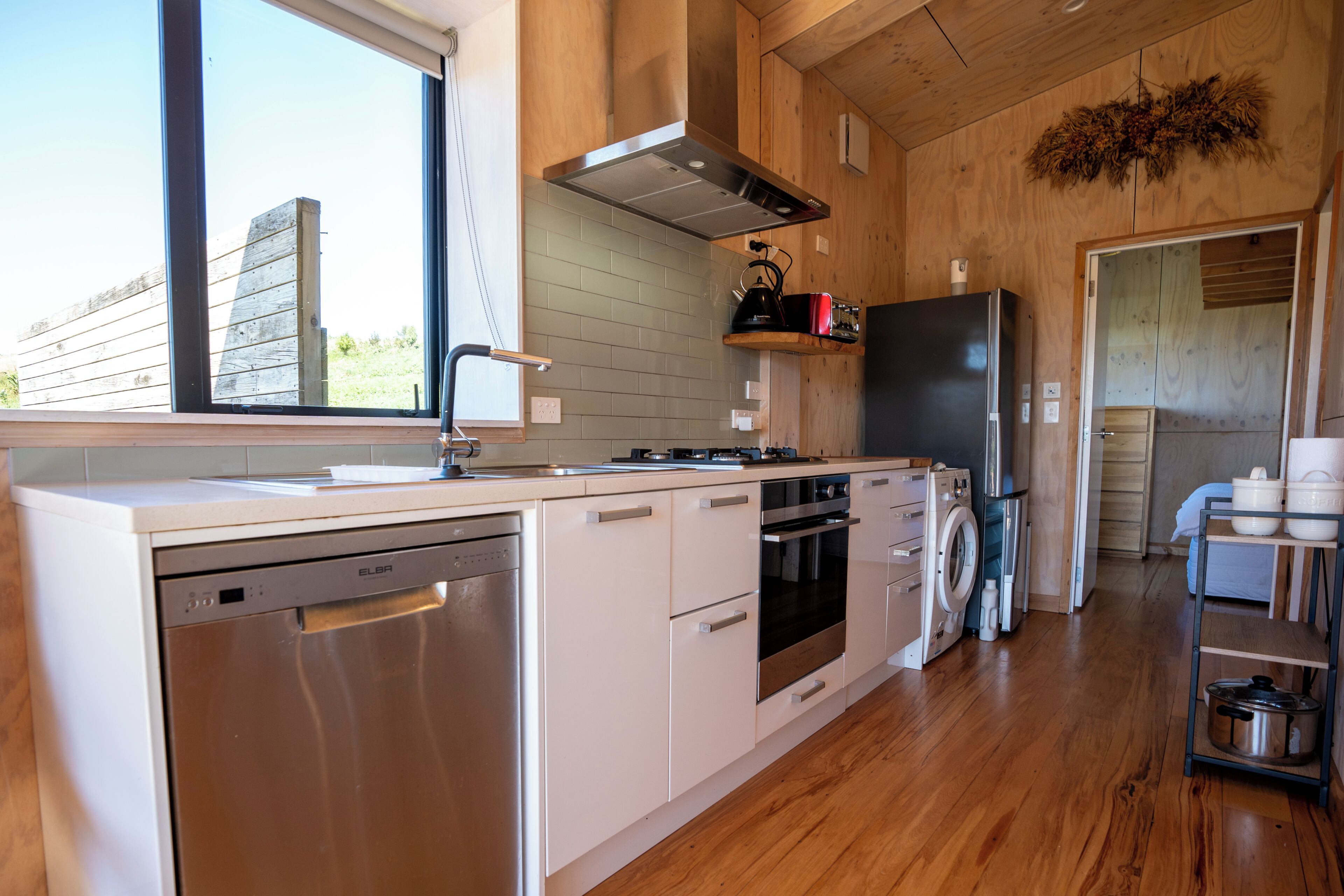 A modern kitchen with wooden cabinetry, stainless steel appliances, and a large window.
