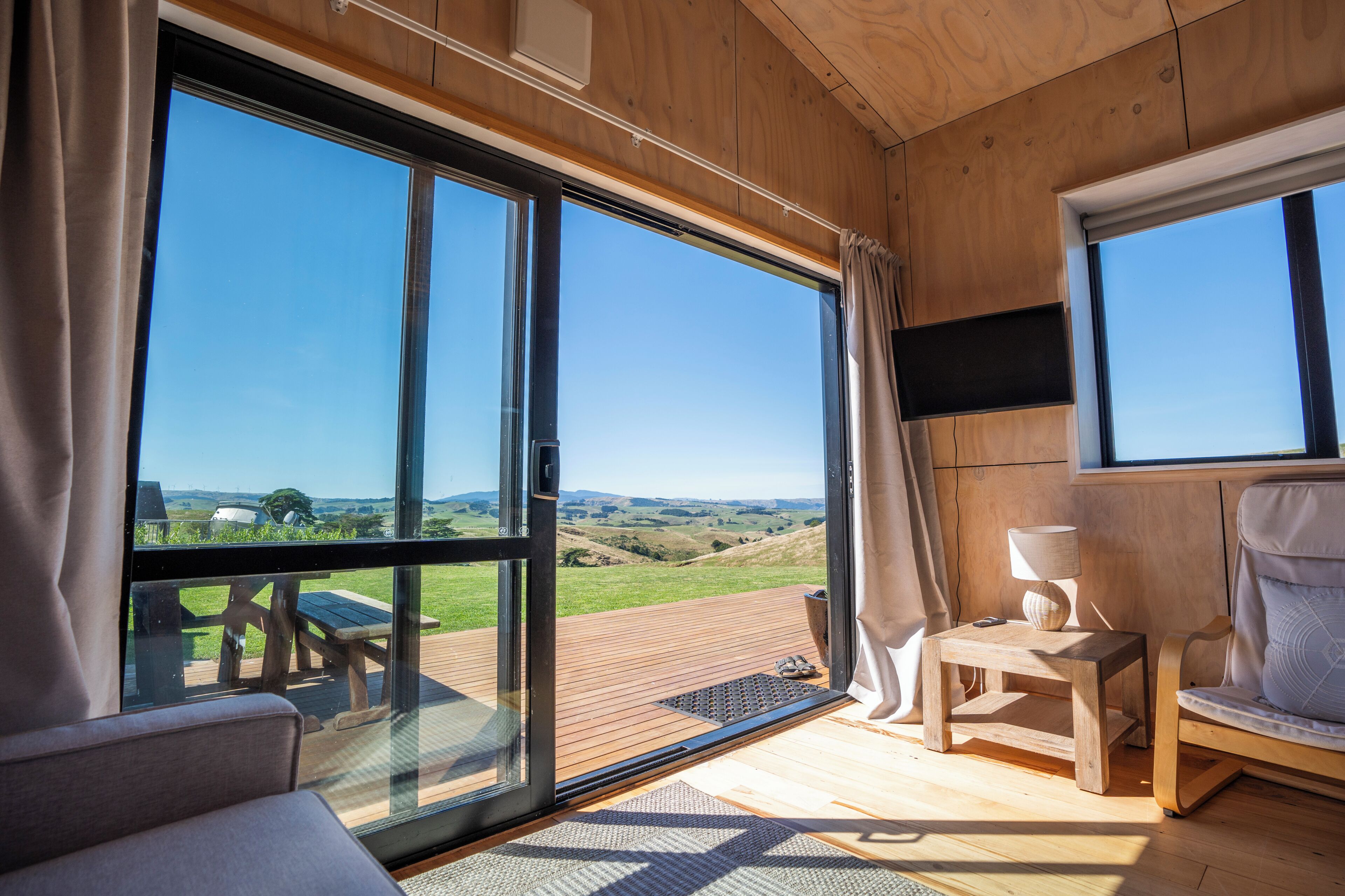 Une pièce dotée de grandes portes-fenêtres coulissantes, d’une terrasse en bois, d’un canapé, d’un fauteuil et d’un téléviseur.