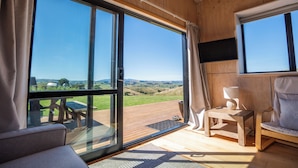 A room with large sliding glass doors, a wooden deck, a sofa, a chair, and a television.