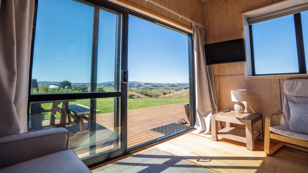 Et værelse med store skydedøre af glas, en træterrasse, en sofa, en stol og et fjernsyn.