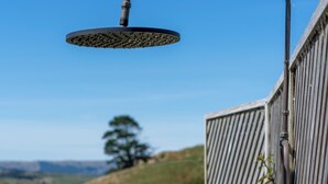 A metal showerhead attached to a wall with a view of a hilly landscape.