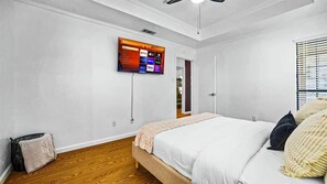 Une chambre à coucher avec un lit, un téléviseur fixé au mur et une porte donnant sur une autre pièce.