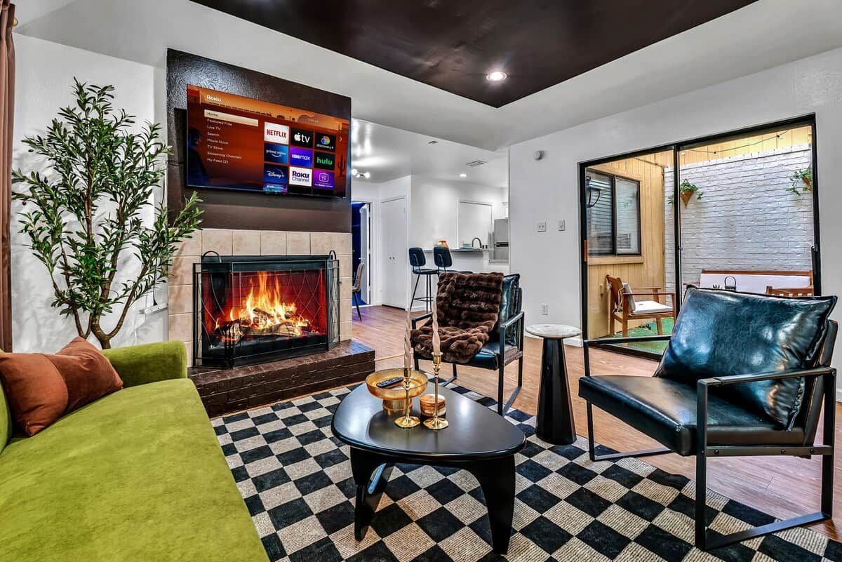 Una sala de estar con chimenea, televisor montado en la pared y piso de cuadros.