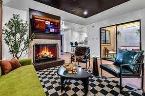 A living room with a fireplace, a television mounted on the wall, and a checkered floor. - Retro Dallas Gem: Game Room + Fire Pit (Dallas)