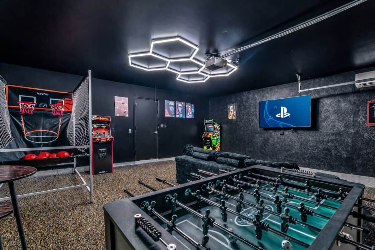 A room with a foosball table, a basketball hoop, and a PlayStation TV.