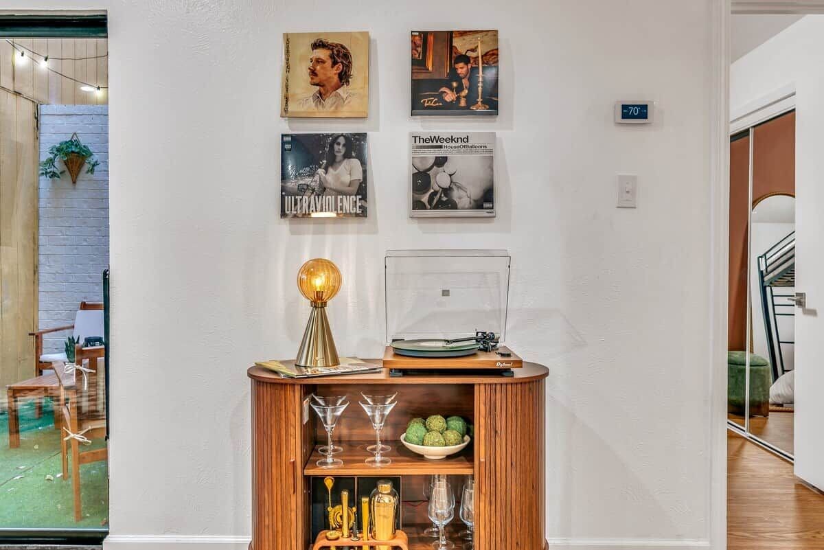 Una habitación con un mueble de madera que exhibe discos y vasos, una pared con cuadros enmarcados y un termostato que indica 21 grados.