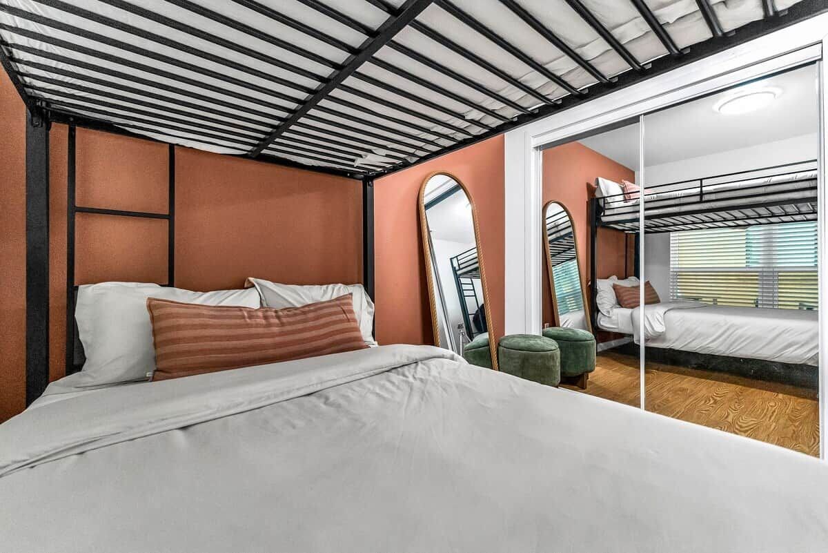 A bedroom with a bunk bed, a large mirror, and a green ottoman.