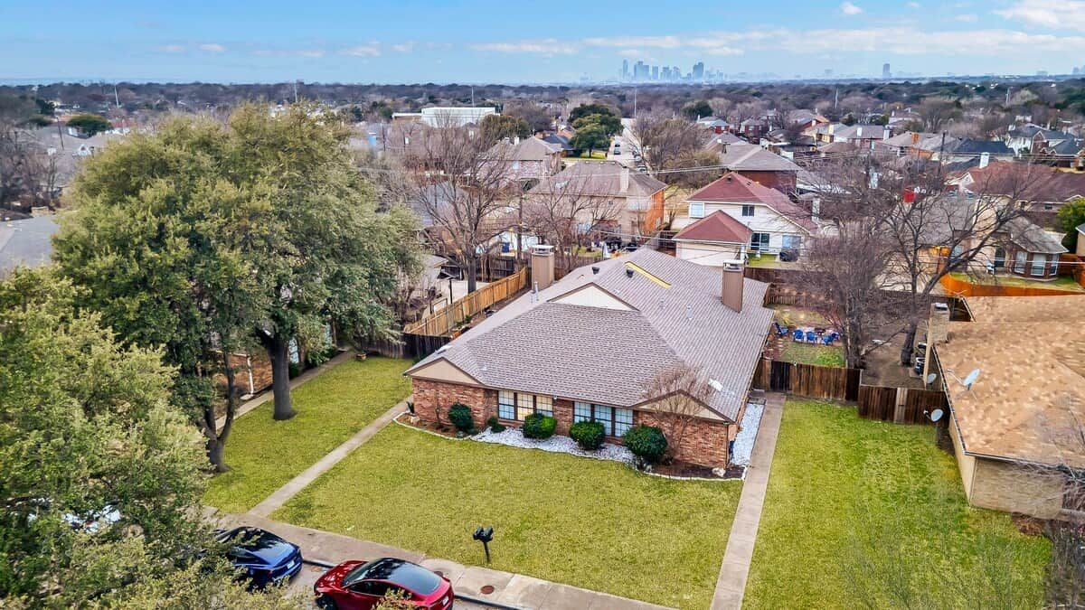 A residential area with houses, a large tree, and parked cars.