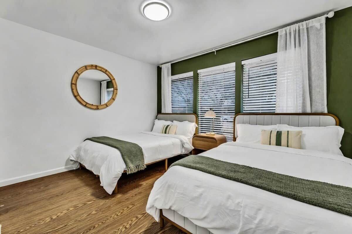 Un dormitorio con dos camas, un espejo redondo y una ventana con persianas.