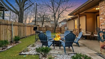 Un patio trasero con un hogar a leña, mobiliario exterior y una valla de madera.