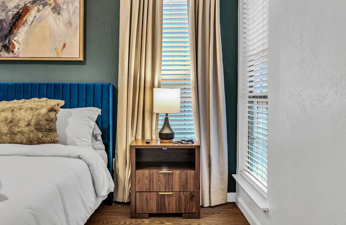 Un dormitorio con cama, mesita de noche, lámpara y ventana con persianas.