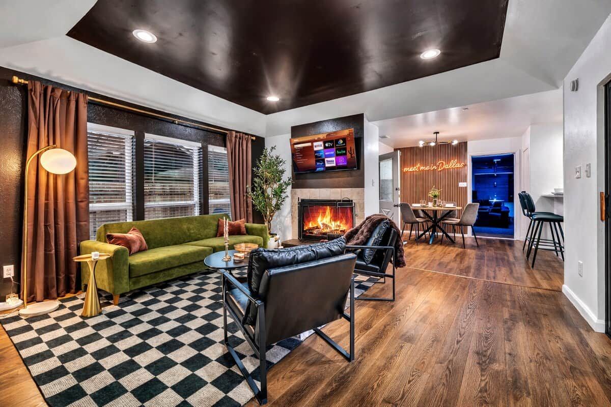 A modern living room with a fireplace, a television mounted on the wall, and a dining area with a table and chairs.