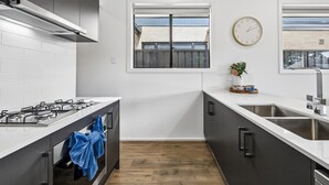 A modern kitchen with a gas stove, stainless steel sink, and a window with a view of buildings. - Modern four bedroom home with everything you could possibly need in a prime coast to city location! (South Plympton)