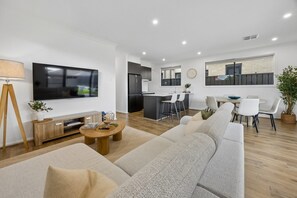 Ein modernes Wohnzimmer mit einem großen Flachbildfernseher, einer Couch, einem Couchtisch und einem Essbereich mit Stühlen und einem Tisch.