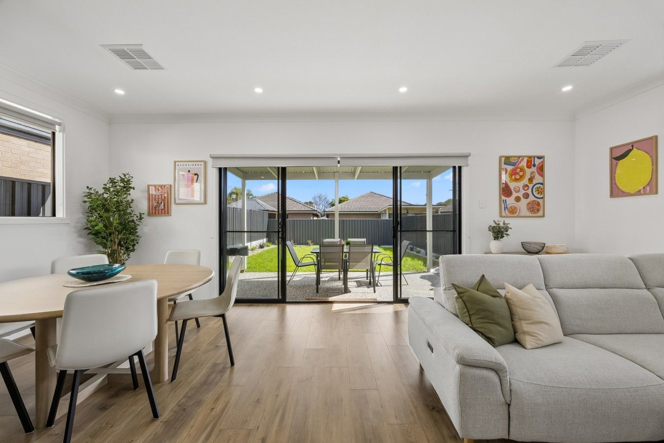 A modern living room with a grey sofa, a dining table with chairs, and a sliding glass door leading to a backyard.