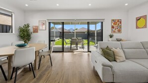 A modern living room with a grey sofa, a dining table with chairs, and a sliding glass door leading to a backyard. - Modern four bedroom home with everything you could possibly need in a prime coast to city location! (South Plympton)