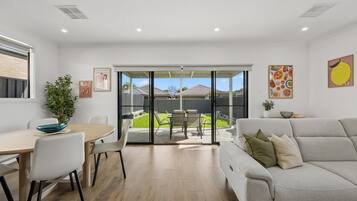 A modern living room with a grey sofa, a dining table with chairs, and a sliding glass door leading to a backyard.