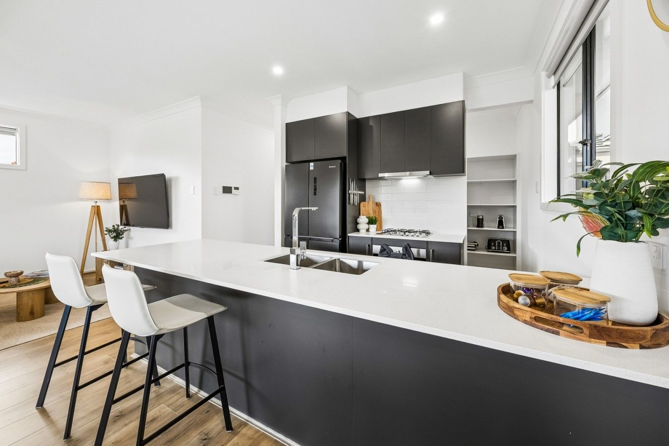 A modern kitchen with a large island, bar stools, and a potted plant.