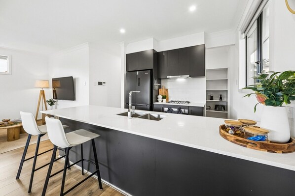 A modern kitchen with a large island, bar stools, and a potted plant.
