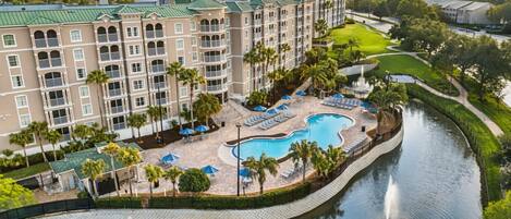 A hotel with a swimming pool, lounge chairs, and palm trees.