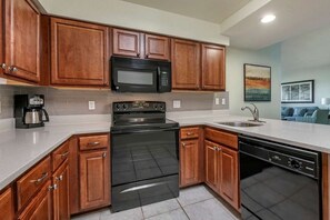 A modern kitchen with wooden cabinets, a black microwave, a stove, and a dishwasher. - Orlando | Friends Theme Park Trip | Pool + Golf | 2BR (Celebration)