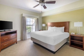 A hotel room with a bed, a television on a wooden dresser, a ceiling fan, and a window with curtains.