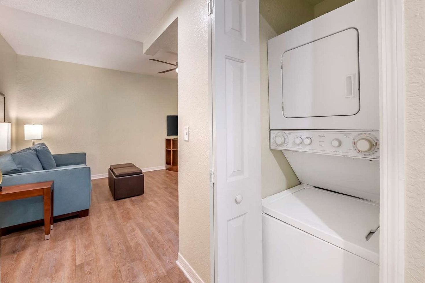 A laundry room with a front-loading washer and dryer, a blue sofa, and a wooden table.
