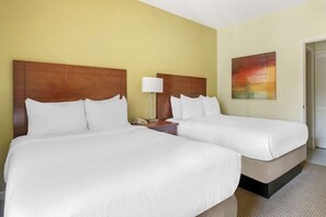 A hotel room with two beds, a nightstand, a lamp, and a painting on the wall.