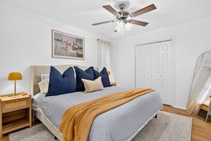 A bedroom with a bed, a ceiling fan, a nightstand, a lamp, a painting, and a wardrobe. - Sunshine Shores-Waterfront Lake Granbury Getaway • Sleeps 10 (Granbury)