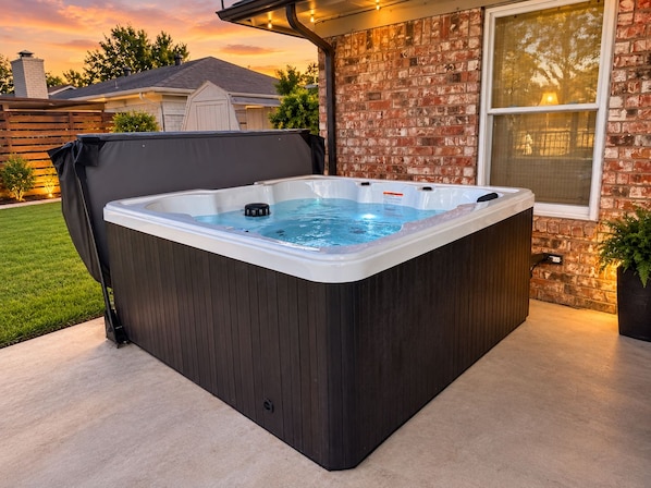 A hot tub in a covered outdoor area with a brick wall and a window. - Sunshine Shores-Waterfront Lake Granbury Getaway • Sleeps 10 (Granbury)
