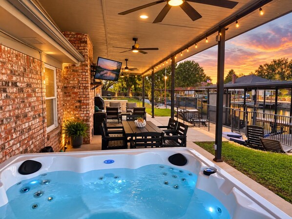 Un patio couvert comprenant un jacuzzi, des sièges d’extérieur et un écran de télévision.