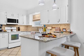 A modern kitchen with white cabinetry, a central island with bar stools, and a tiled backsplash. - Sunshine Shores-Waterfront Lake Granbury Getaway • Sleeps 10 (Granbury)