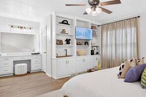 Une chambre à coucher comprenant un lit, un bureau, une armoire, un téléviseur et un ventilateur de plafond.
