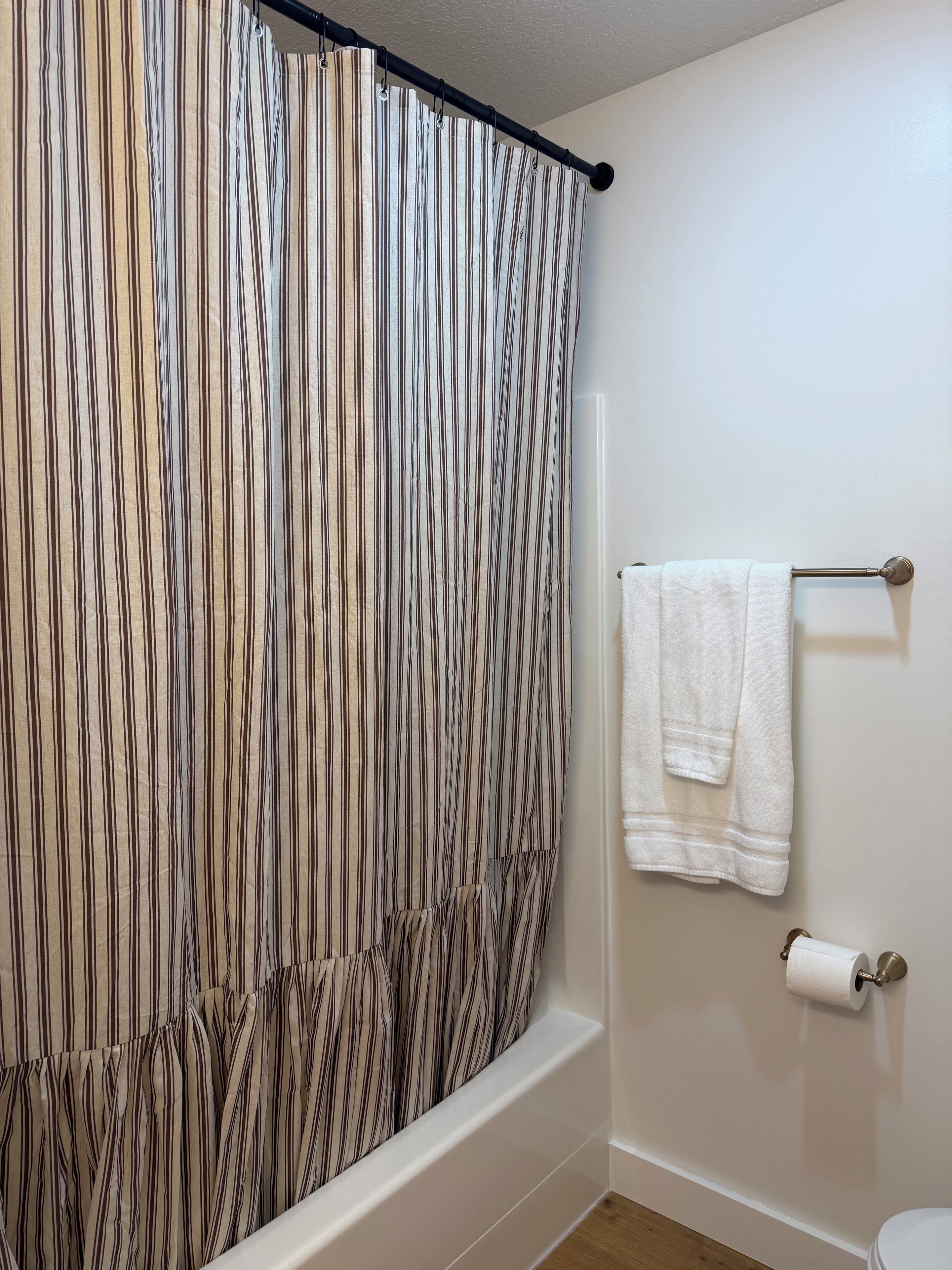 Un bagno con tenda da doccia a righe, un portaserviti bianco con asciugamani e un porta rotolo per carta igienica.