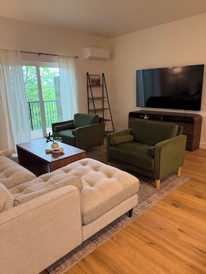 A living room with a sofa, armchairs, a coffee table, a TV, and a ladder against the wall.